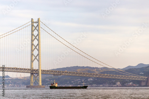 Cargo ship cruising under suspension bridge at sunset