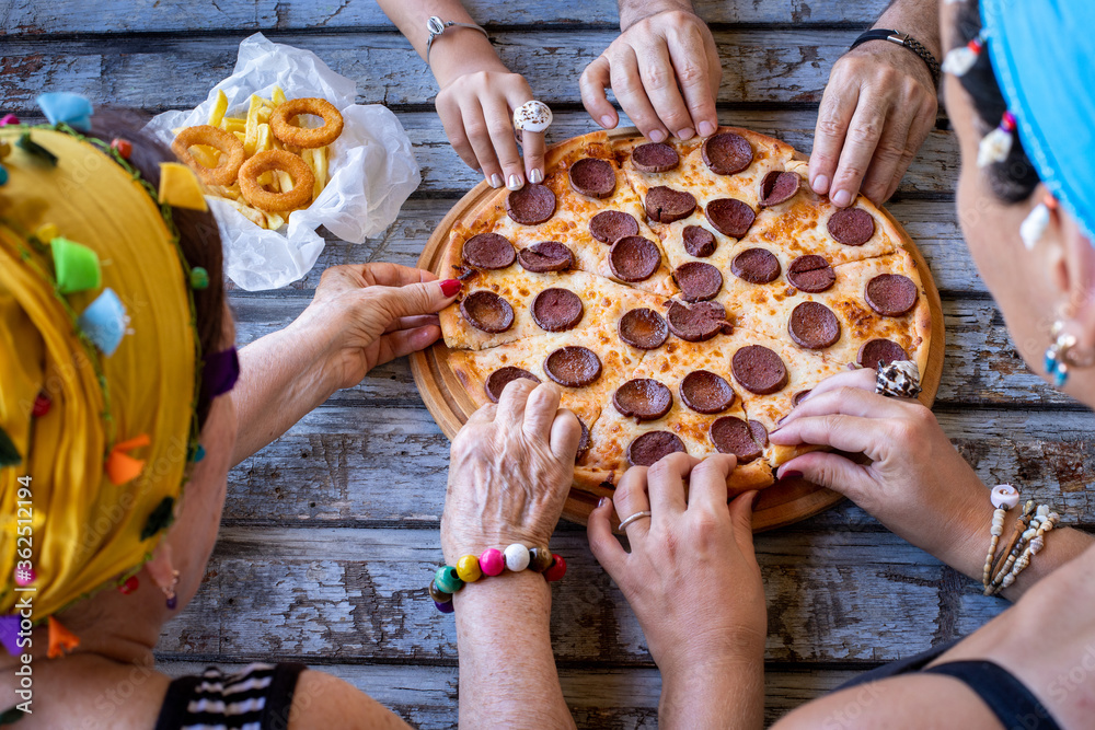 Many hands and side view of two women who are eating pizza on the table