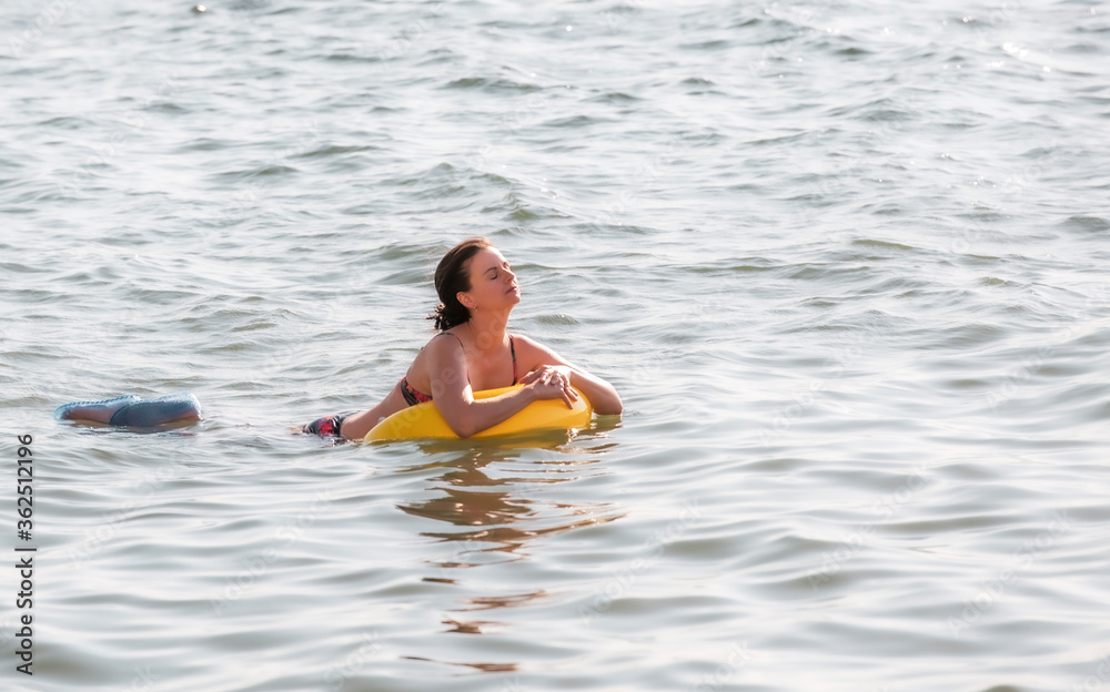 A brunette woman swims in the sea on a swimming circle.