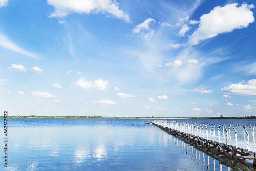 Blue sky with light clouds, blue water and white pier in the sunny summer day.