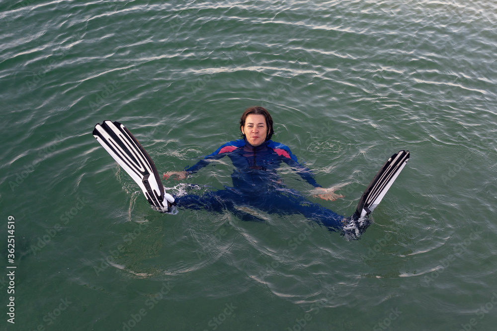 Obraz premium Beach vacation fun woman wearing a wetsuit and flippers making a goofy face while swimming in ocean water