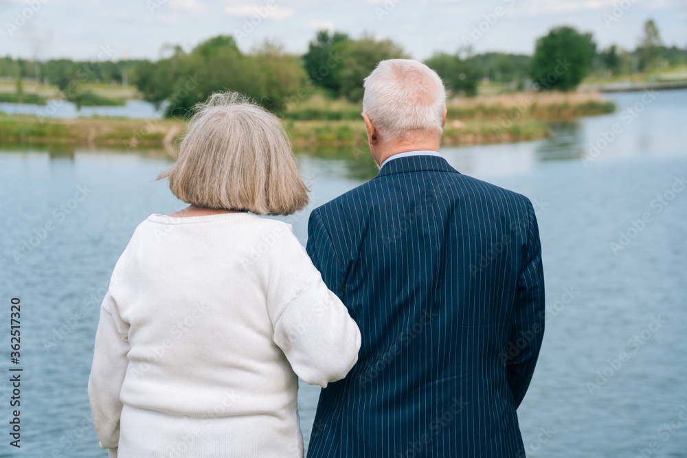 Portrait of an elderly man and woman stand with their backs on the background of a blue lake.