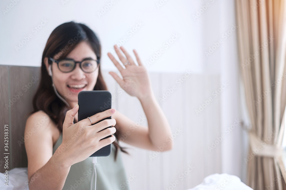 Happy casual woman making video calling by smartphone at home, young adult asian female using meeting online app on bed. social distancing, new normal, work from home, remotely and technology concept Happy casual woman making video calling by smartphone at home, young adult asian female using meeting online app on bed. social distancing, new normal, work from home, remotely and technology concept