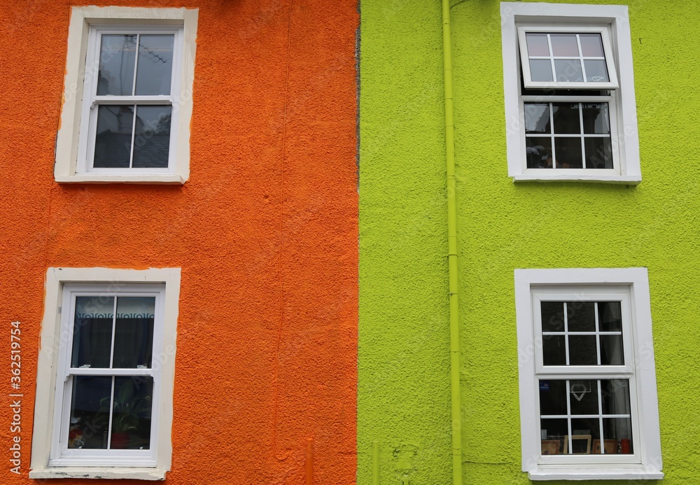 Brightly coloured orange and green fluorescent walls with symmetrical windows on adjacent British cottages.
