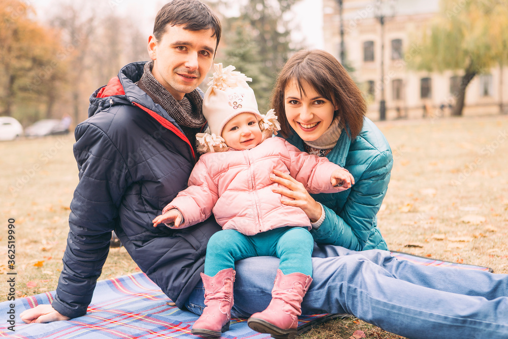 Casual family couple with daughter on a free time in park. Autumn cloudy weather with fallen leafs. Copy space