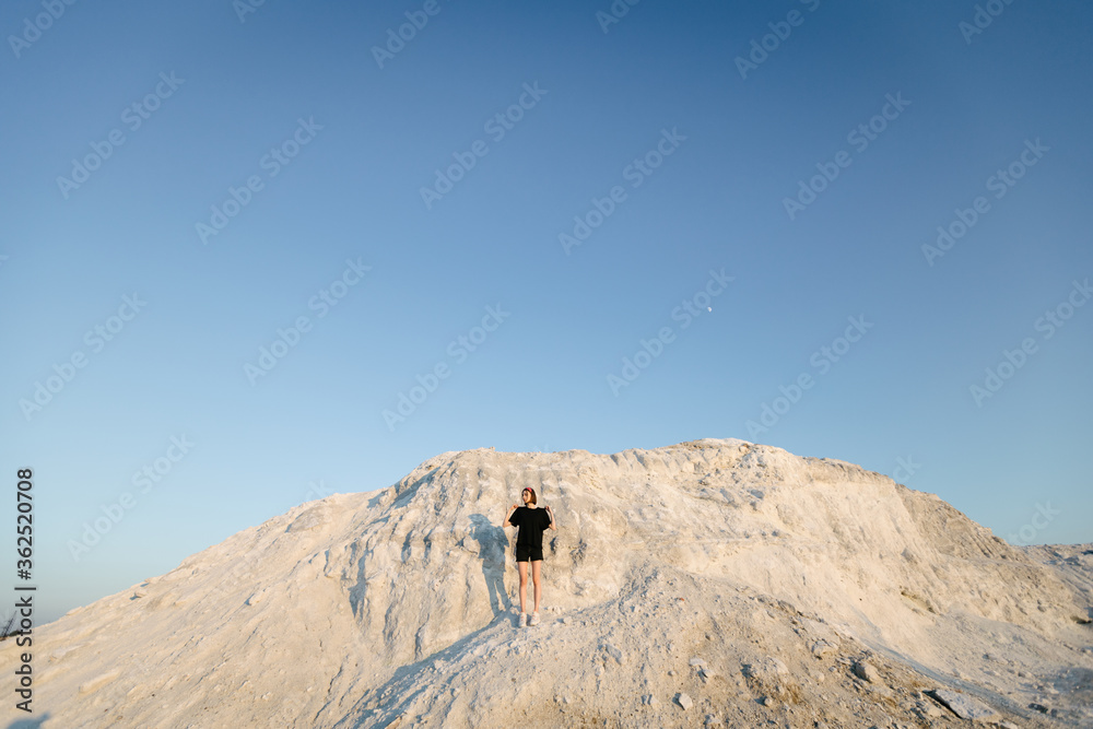 Slim beautiful girl at sunset over white mountain looking at the sun in the summer