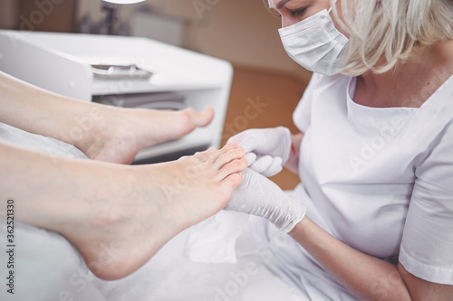 Pedicurist doing professional medical pedicure procedure in beauty salon with special eguipment. Foot treatment in SPA salon. Podiatry clinic. Beautician doctor hands in white gloves with female legs photo