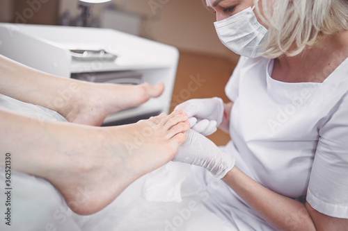 Pedicurist doing professional medical pedicure procedure in beauty salon with special eguipment. Foot treatment in SPA salon. Podiatry clinic. Beautician doctor hands in white gloves with female legs