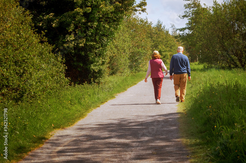 Old couple walking on a foot path on a warm sunny day. Concept active lifestyle.