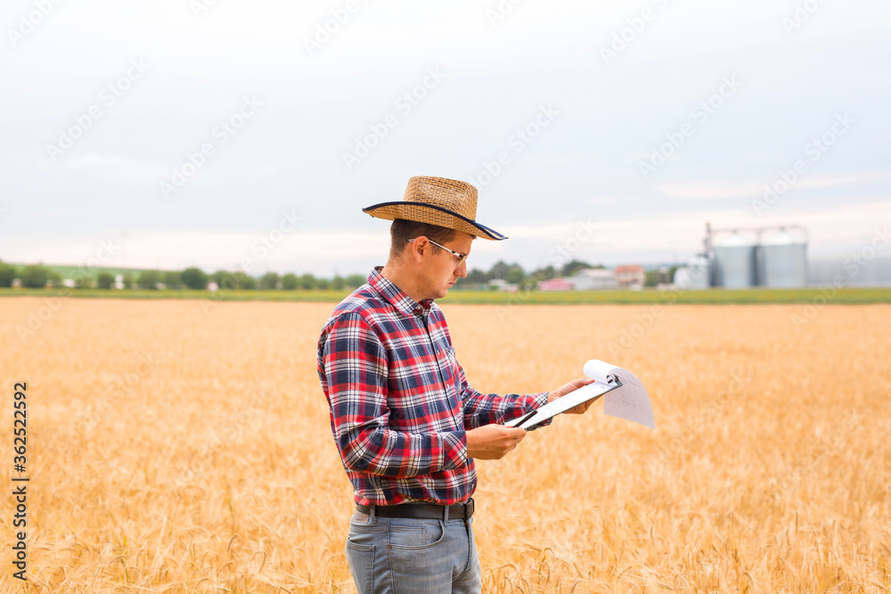 Young Farmer writing on a document the wheat development plan. Farmer checking wheat field progress. Copy space.