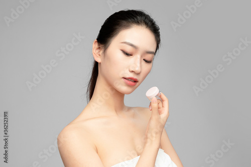 Close-up face of beautiful Asian woman holding plastic vial in hand as display in grey background
