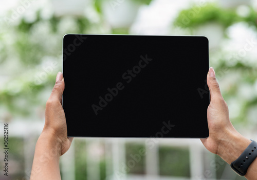 Industrial cultivation of potted plants with modern technology. Hands of african american girl with smartwatch holding tablet with empty screen on greenhouse background