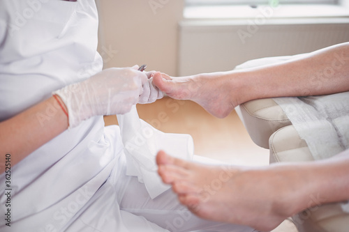 Professional medical pedicure procedure close up using nail clippers instrument. Patient visiting chiropodist podiatrist. Foot treatment in SPA salon. Podiatry clinic. Pedicurist hands white gloves.