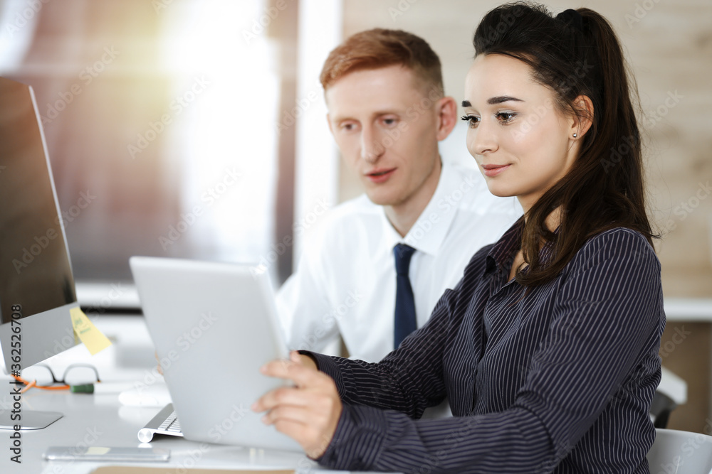 Business woman and man discussing questions while using tablet computer in sunny office. Teamwork, meeting and brainstorming concept Business woman and man discussing questions while using tablet computer in sunny office. Teamwork, meeting and brainstorming concept
