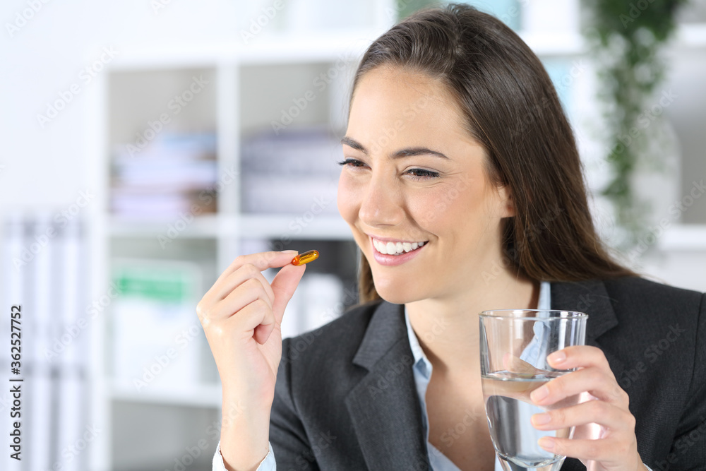 Happy executive takes vitamin pill with water at office Happy executive takes vitamin pill with water at office