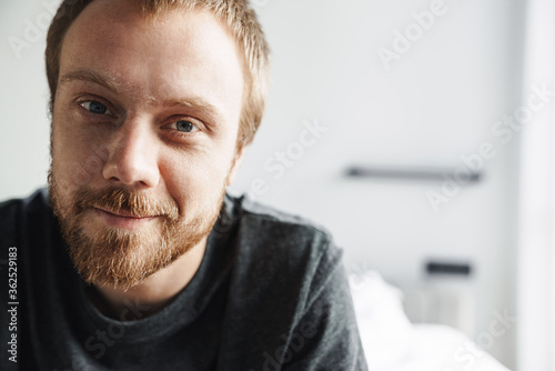 Photo closeup of joyful man smiling at camera while sitting on bed