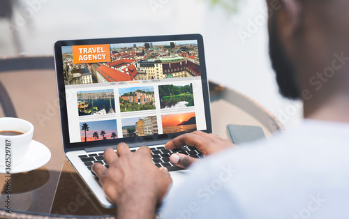 Black Man Using Travel Agency Website On Laptop While Sitting In Cafe