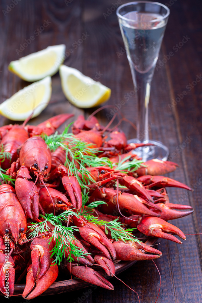 Crayfishes on plate served with dill, lemon and glass of schnapps, dark wooden background, vertical Crayfishes on plate served with dill, lemon and glass of schnapps, dark wooden background, vertical