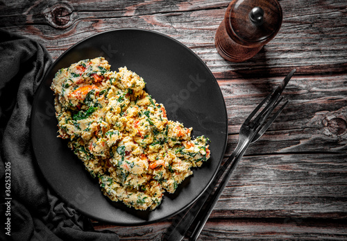 scrambled eggs with spinach and tomato in plate on wooden table background