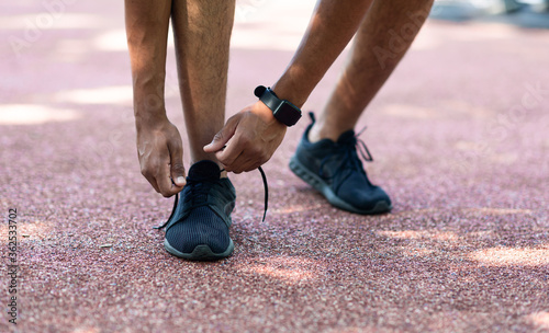 Millennial sportsman tying laces of his shoes on jogging track  closeup of legs