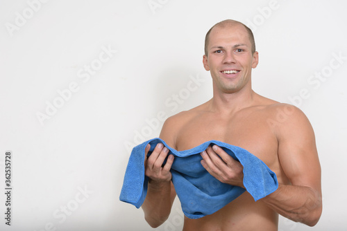 Happy young muscular bald man using face towel shirtless