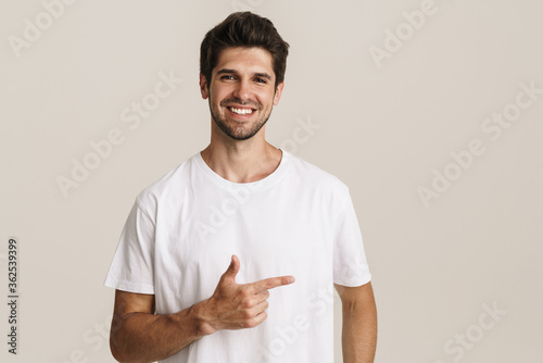 Portrait of joyful young man smiling and pointing finger aside photo