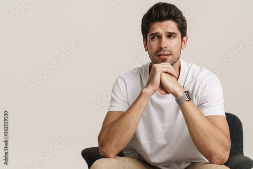 Portrait of unshaven young man looking aside while sitting on armchair