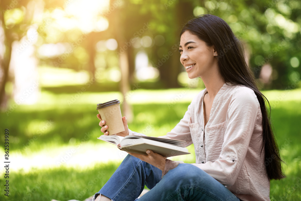 Obraz premium Young asian girl reading book and drinking takeaway coffee in park outdoors