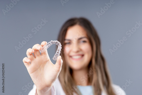 Beautiful smiling Turkish woman is holding an invisalign bracer in a grey background studio with copy space