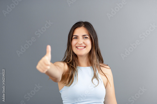 Beautiful brunette Turkish woman making an okay gesture with her hand, grey background studio shot with copy space