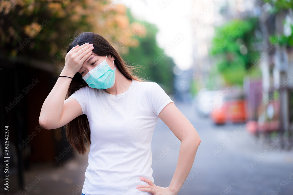 Concept of concern about virus outbreak and air pollution. Woman uses her forehead to grasp the anxiety and dizziness. Measure body temperature. Working women upset. Wearing a green medical face mask.