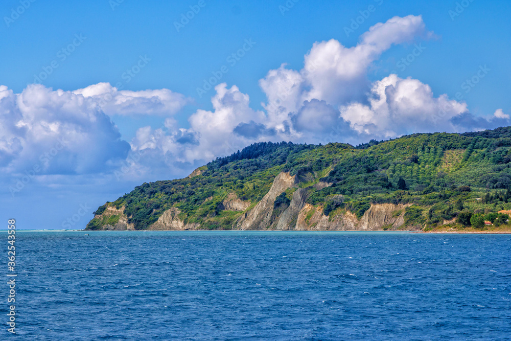 Seascape with blue water, mountain, covered with green trees and bushes, blue sky with white clouds.