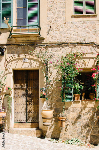 Entrance of an old house in Italy or Spain. Wooden doors, potted flowers, colored windows, sunlight. Travel and walking.  