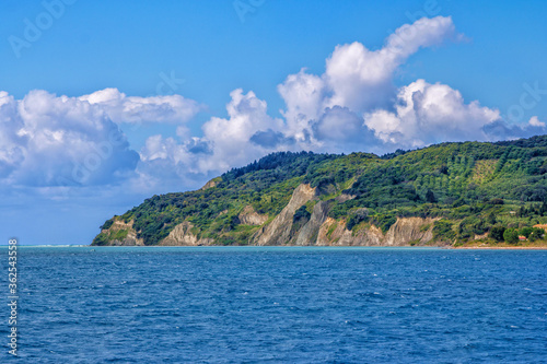 Seascape with blue water, mountain, covered with green trees and bushes, blue sky with white clouds.