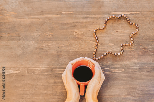 Hands holding a red coffee cup on a wooden table with a cloud made of coffee beans