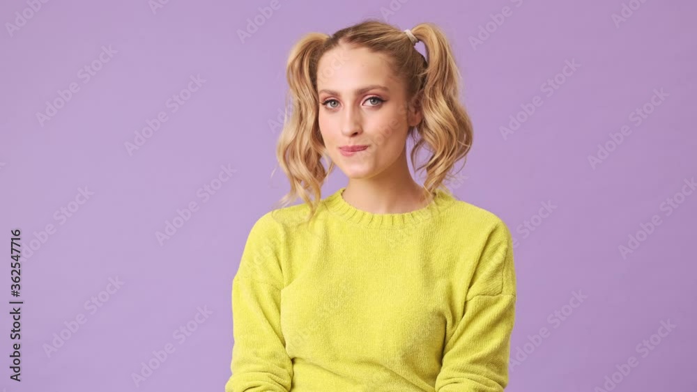 A cute blonde smiling, flirting at the camera, biting her lip and raising eyebrows in an isolated studio on a purple background A cute blonde smiling, flirting at the camera, biting her lip and raising eyebrows in an isolated studio on a purple background