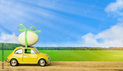 Photography Retro car carrying an easter egg on the roof on green field and blue sky landscape background
