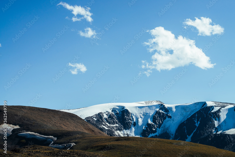 Awesome view to big snowy mountains behind green hill. Great glacier under blue sky. Wonderful vivid highland scenery with giant mountains with snow. Beautiful alpine landscape with glacial mountains.