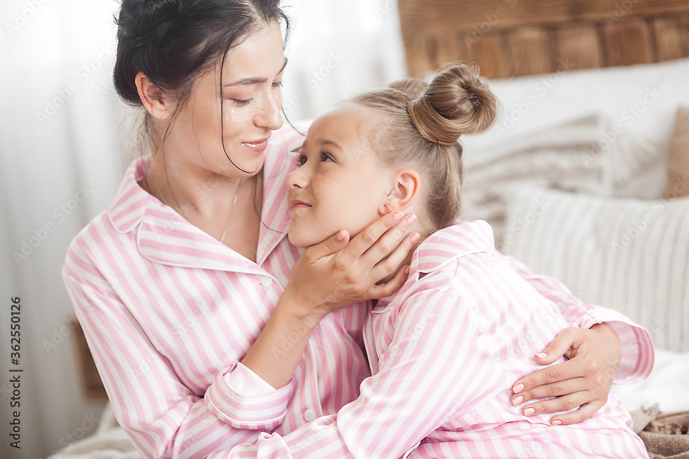 Young active mother and her little daughter having fun together at home in the bedroom wearing pajamas Young active mother and her little daughter having fun together at home in the bedroom wearing pajamas