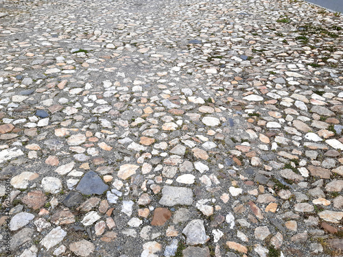 old rural stone paving urban square made of quartz boulders the size of about 15cm joints filled with gravel brown beige white yellow color of pebbles grassy path overgrown  photo