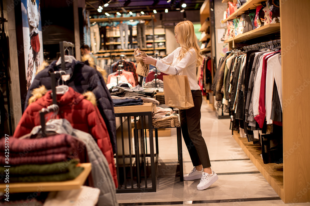 Young woman shopping and searching among clothes at clothes store