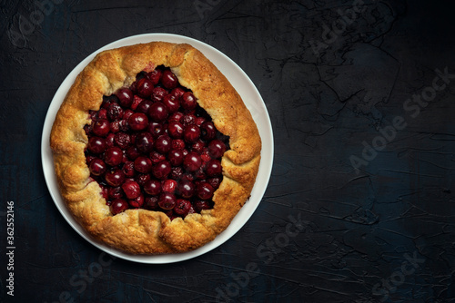 Galette with ripe red cherry filling on dark blue background. Homemade sweet open pie. Space for text. Top view.
