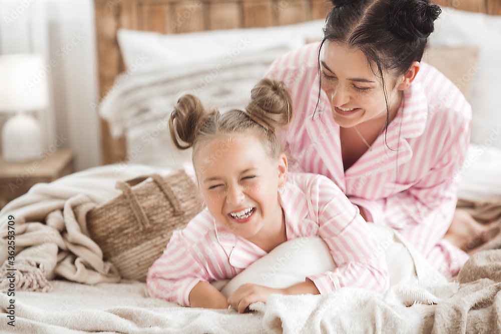 Young active mother and her little daughter having fun together at home in the bedroom wearing pajamas Young active mother and her little daughter having fun together at home in the bedroom wearing pajamas