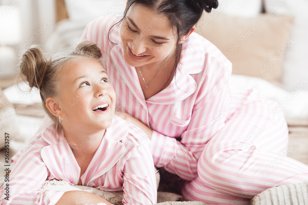 Young active mother and her little daughter having fun together at home in the bedroom wearing pajamas Young active mother and her little daughter having fun together at home in the bedroom wearing pajamas
