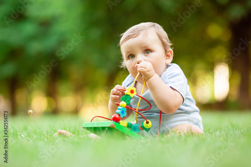 Healthy toddler plays with developing toy sitting on summer grass