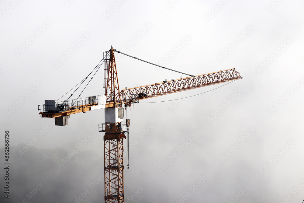 Construction crane in a fog on background of mist sky. Housing construction, real estate business