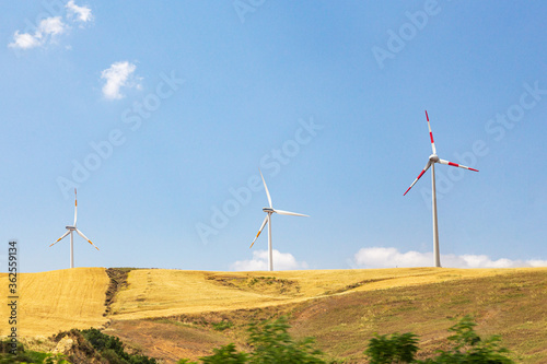 Three wind-driven electric generators against a yellow field and blue sky. Summer sunny day.
