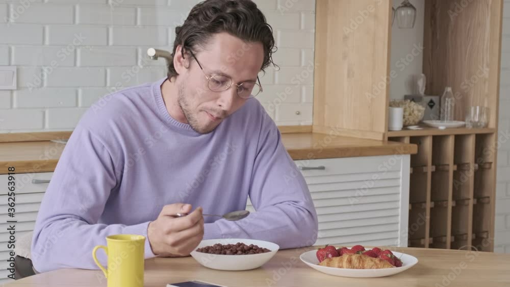 Calm handsome man in eyeglasses having breakfast by the table at home Calm handsome man in eyeglasses having breakfast by the table at home