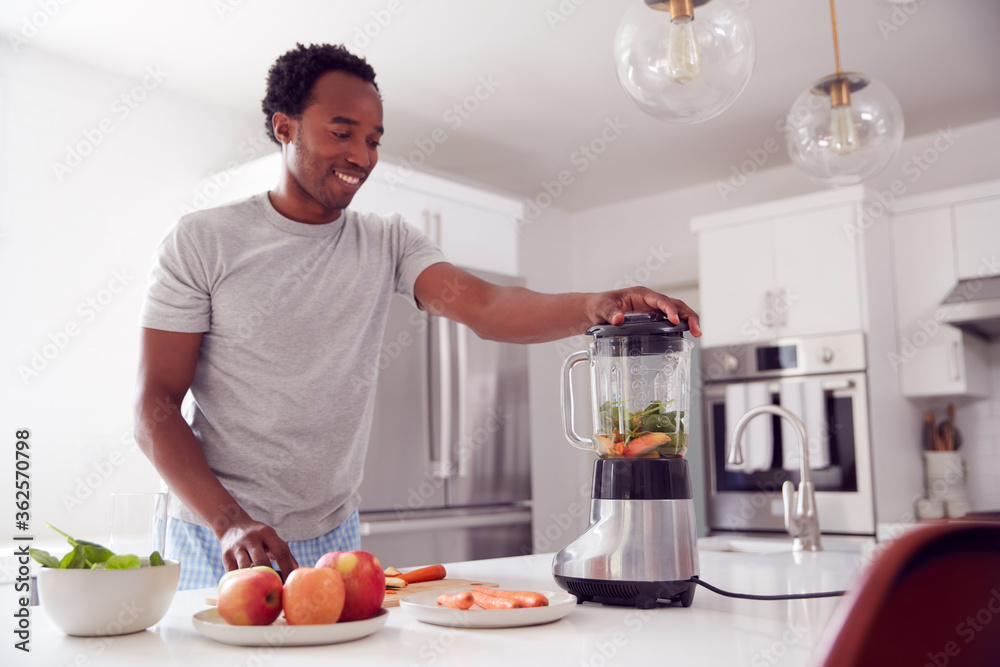 Man Wearing Pyjamas Standing In Kitchen Putting Fresh Fruit And Vegetables Into Blender Man Wearing Pyjamas Standing In Kitchen Putting Fresh Fruit And Vegetables Into Blender