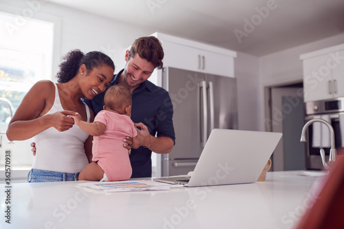 Valokuva Family With Baby Daughter In Kitchen Using Laptop On Counter